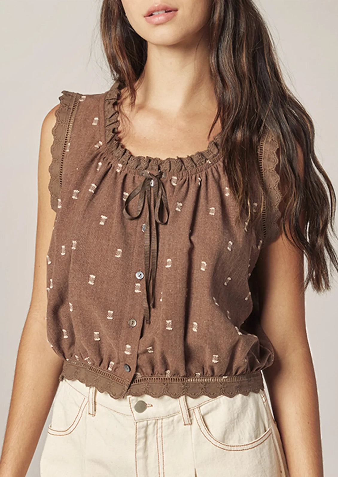 A person wearing a brown sleeveless top with white swiss dot detailing.