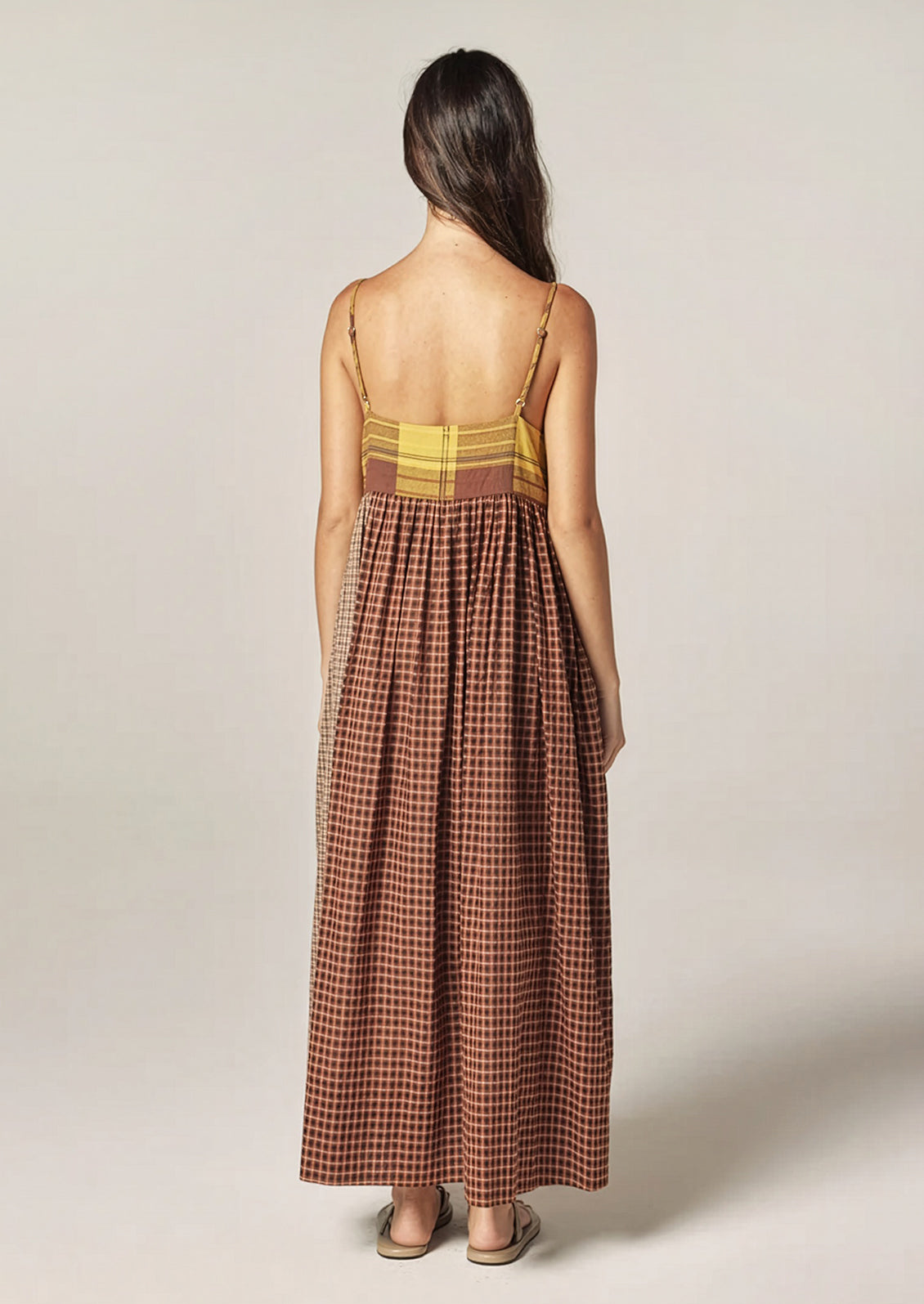 A person wearing a long plaid cotton dress in brown and yellow tones.