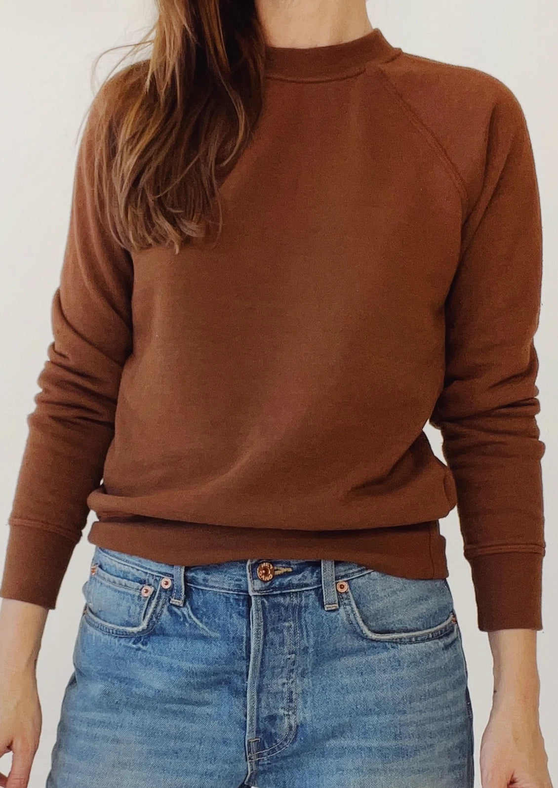 A person wearing a fitted crewneck fleece sweatshirt in cedar brown.