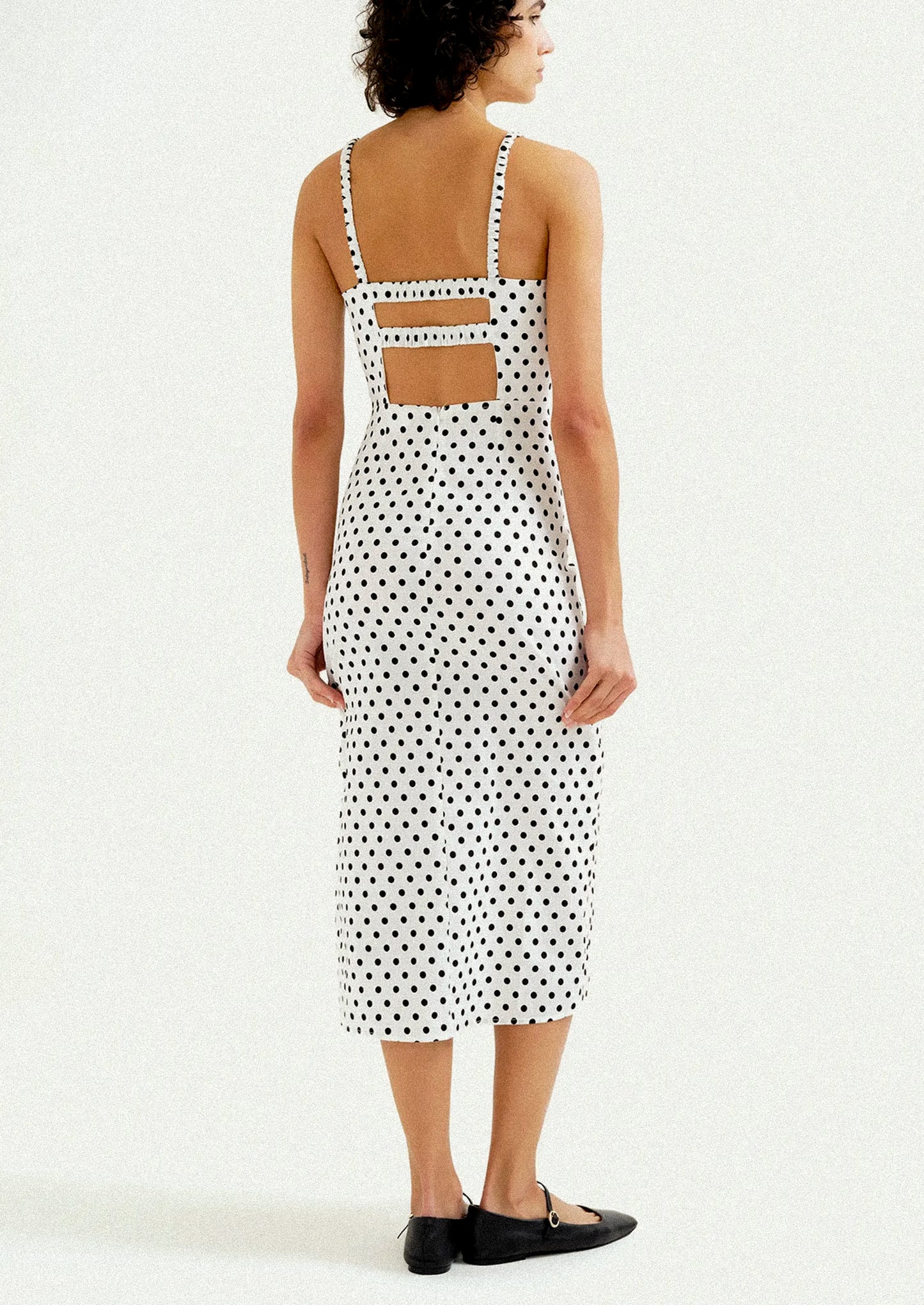 A woman wearing a midi dress in white with black polka dots.