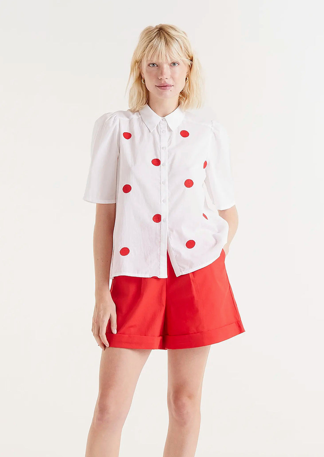 A woman wearing a short sleeve cotton blouse with slight puff sleeve and embroidered red dot pattern.