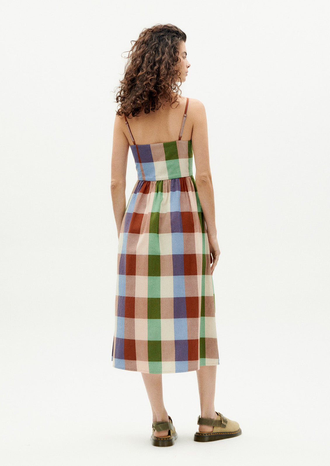 A woman wearing a thin strap dress with straight neckline, in colorful madras cotton.