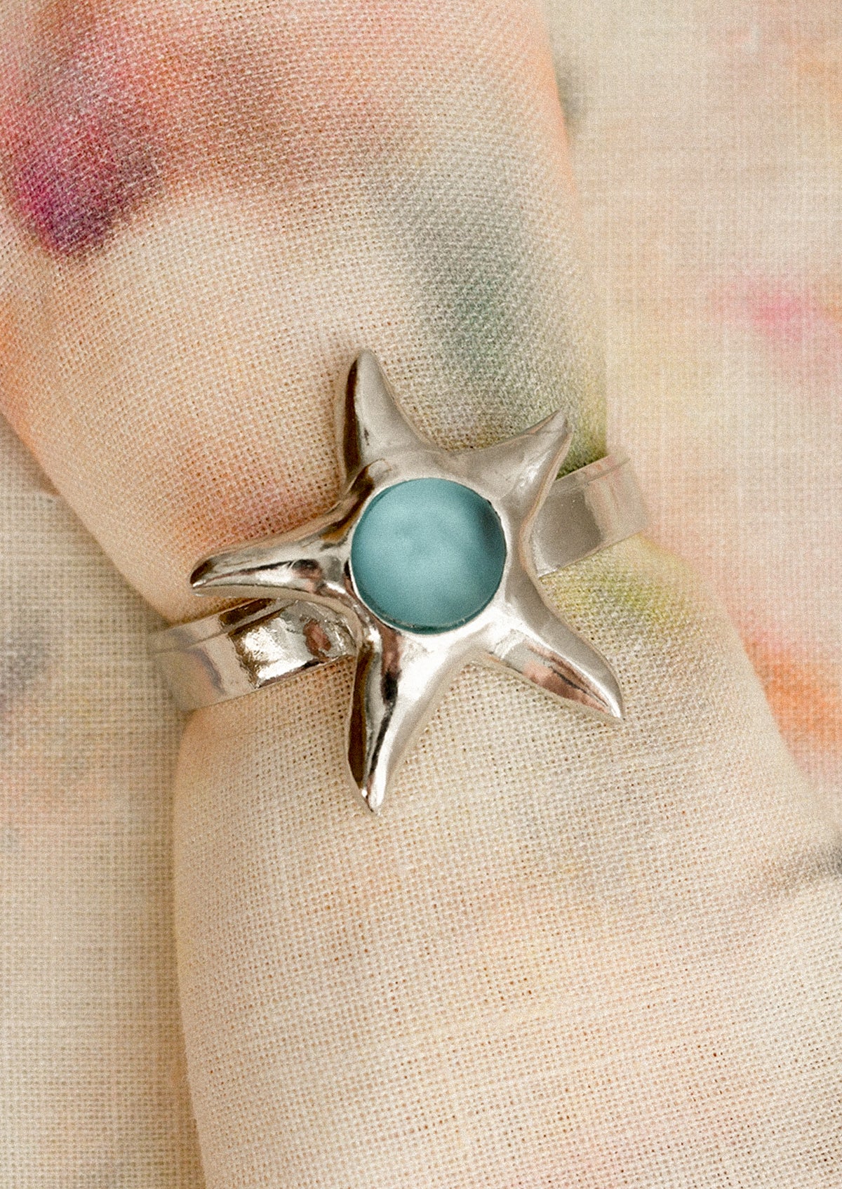 Silver napkin ring with a blue seaglass detail on a floral fabric background
