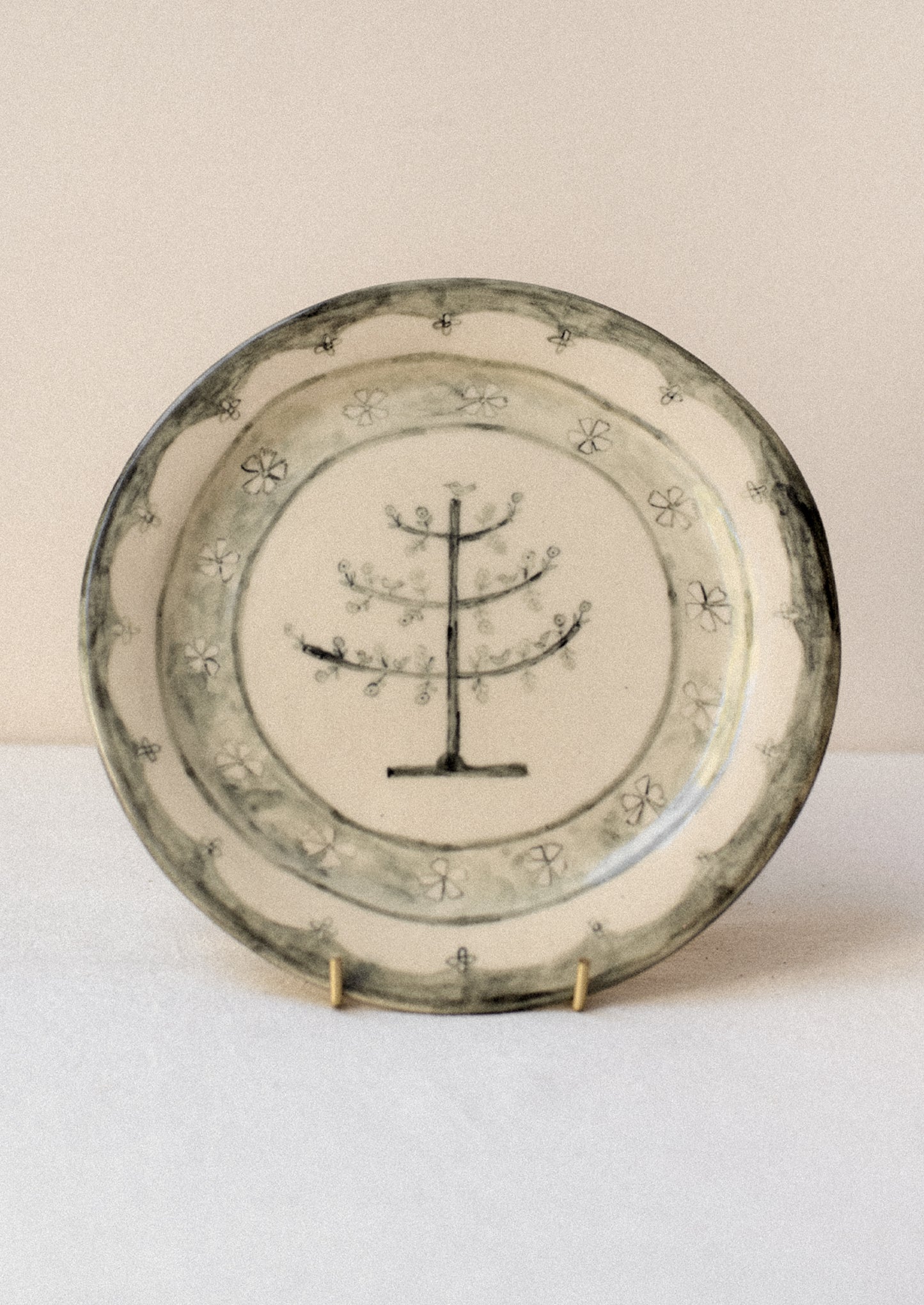 A cream ceramic plate with illustrated tree and flowers in dark grey.