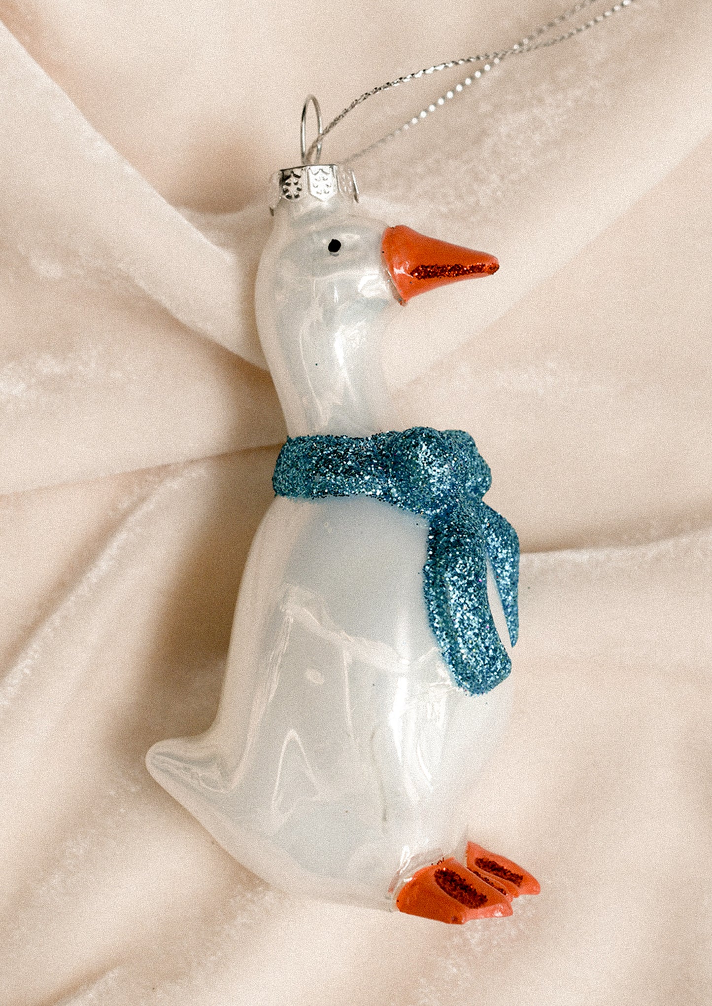 A glass ornament of a white goose wearing blue bow ribbon around its neck.