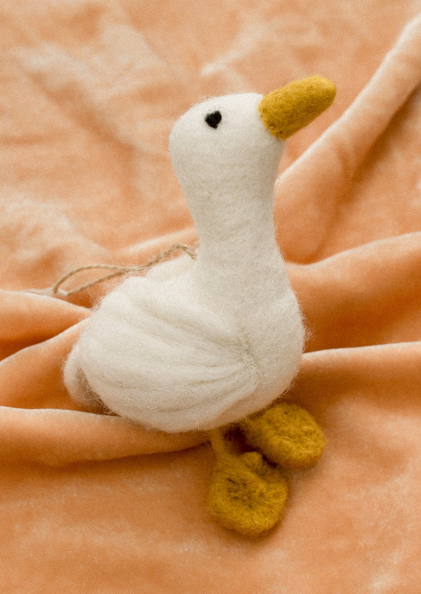 A white felt bird ornament with yellow feet and beak.