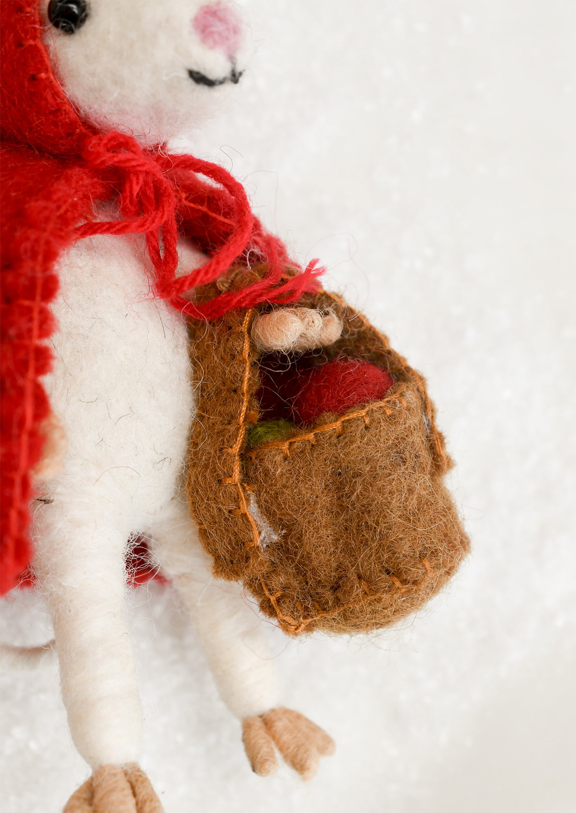 A felted wool ornament of a white mouse dressed as red riding hood, holding a basket.