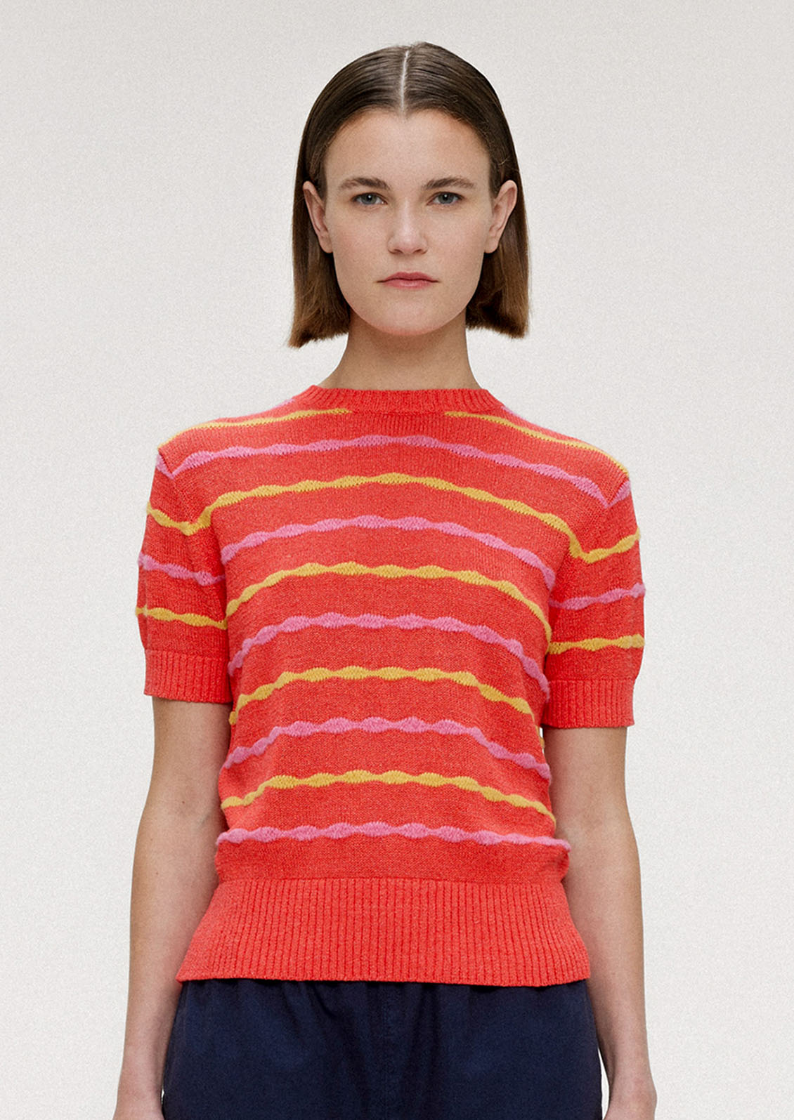A woman wearing a red short sleeve knit top with yellow and pink wavy stripes.