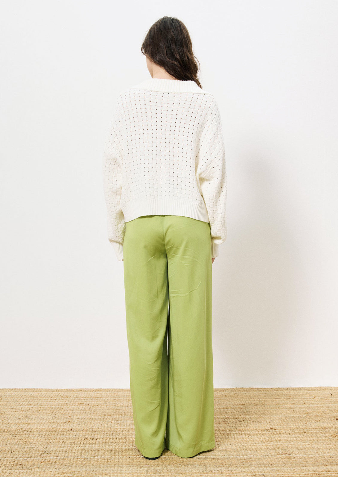 A woman wearing a collared v-neck sweater with woven texture in white.