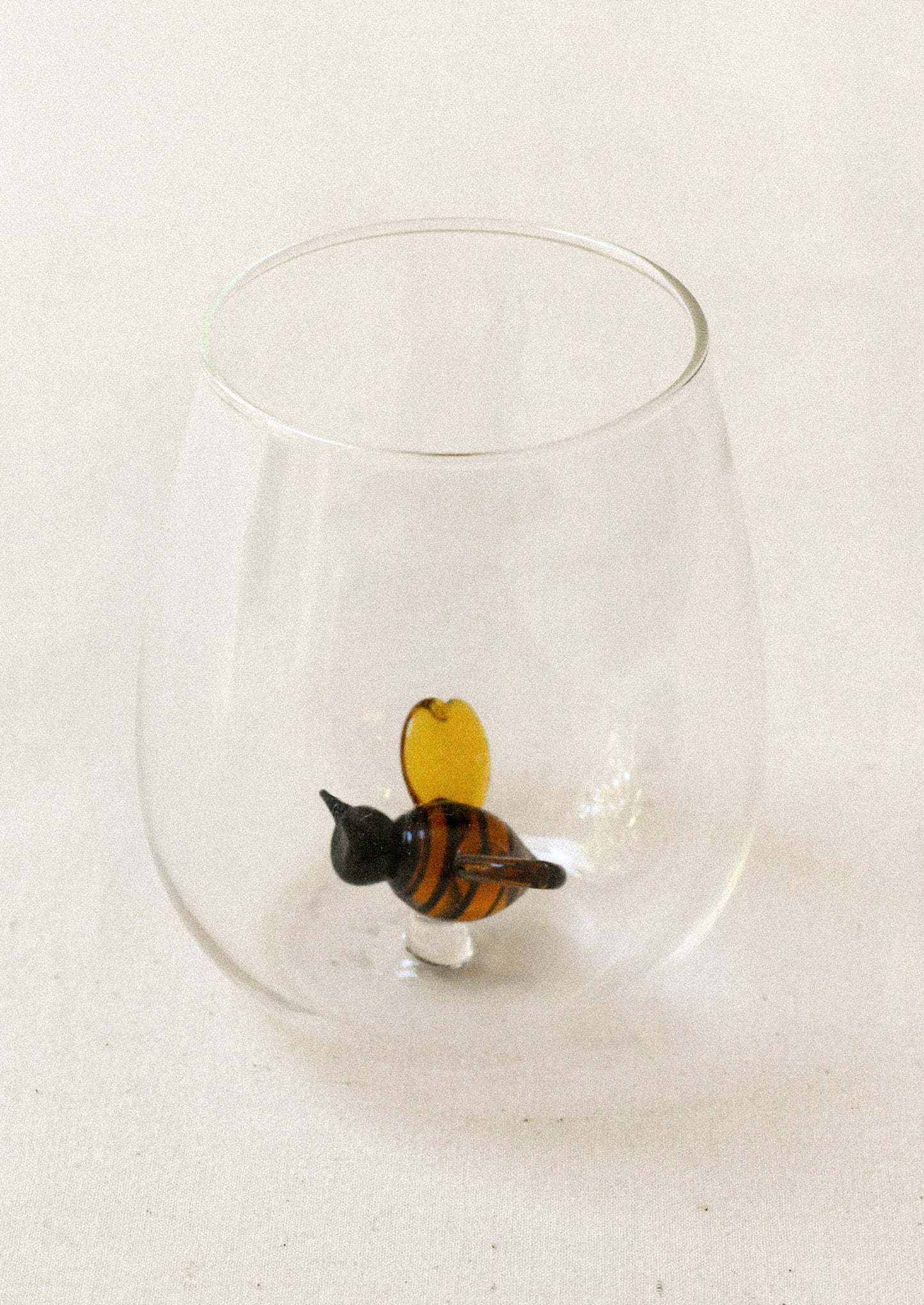 A clear tumbler glass with lampwork bumble bee detail at inner bottom.