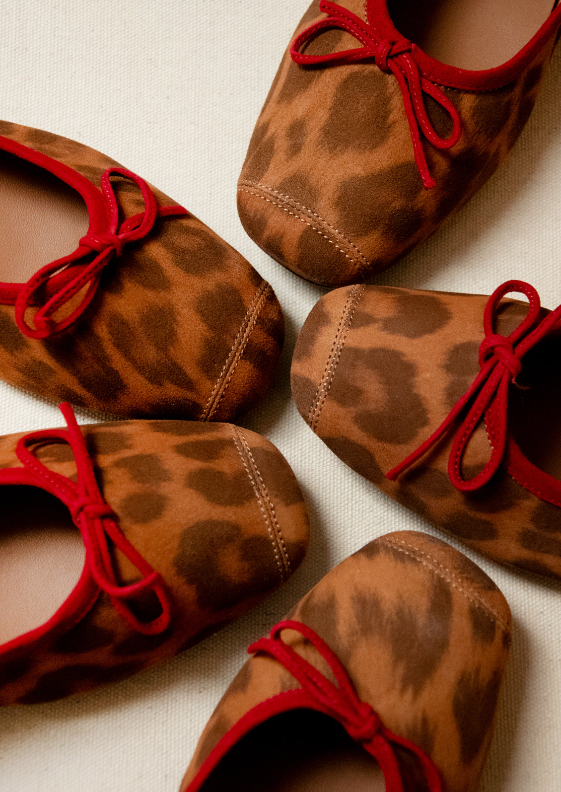A pair of leopard print suede ballet flats with red accent.