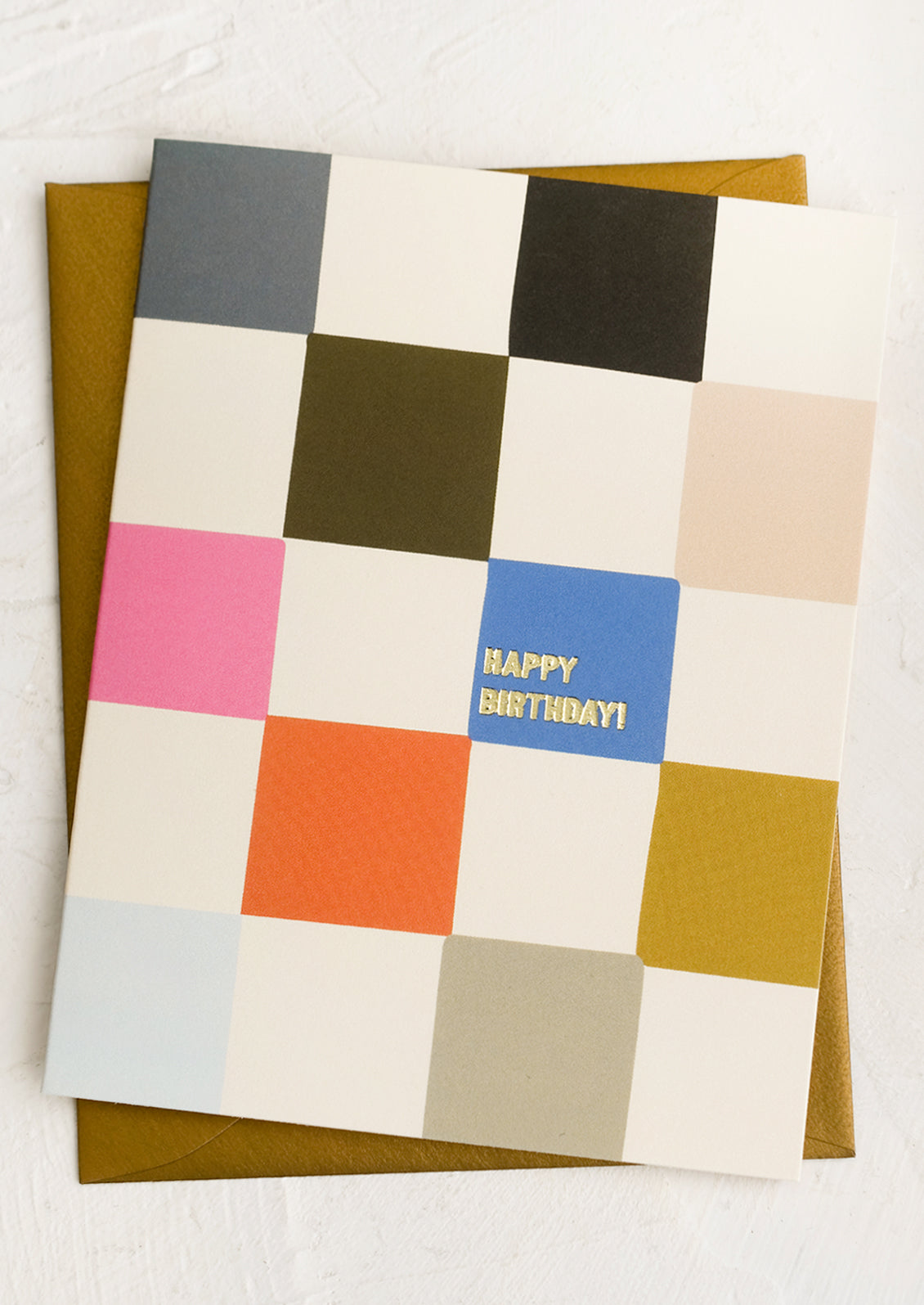 A multicolor checker print greeting card with gold text reading "Happy Birthday!".