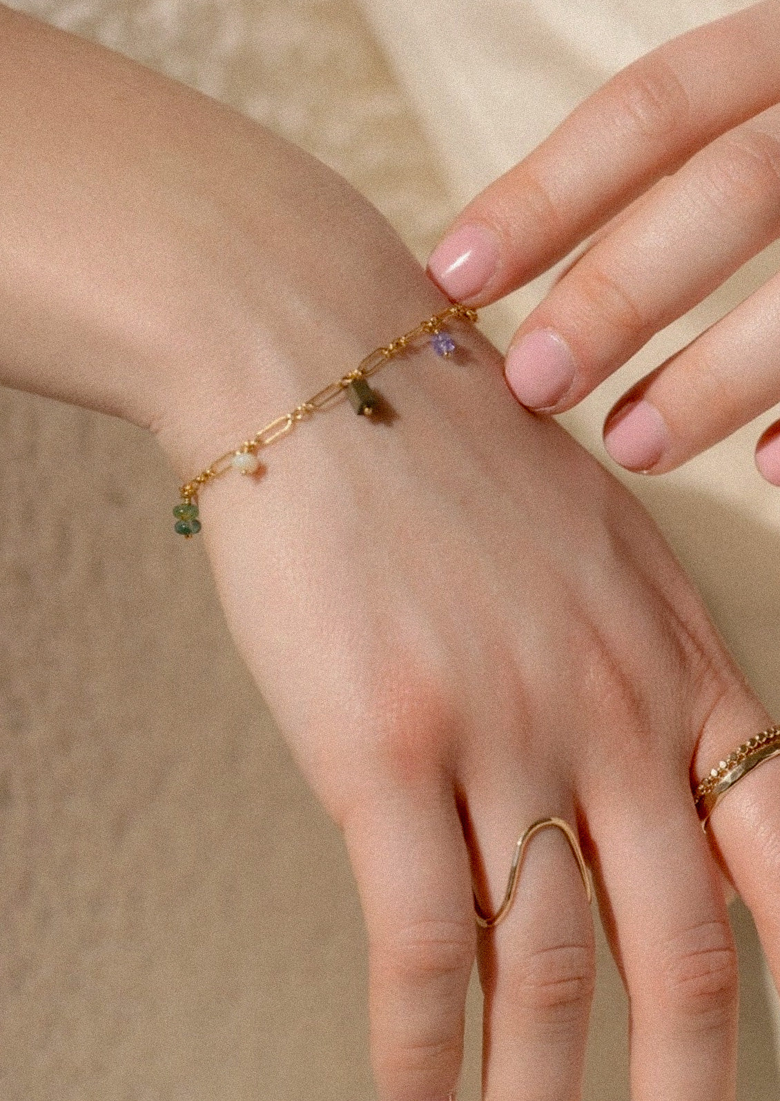 A woman wearing a gold chain bracelet with various colored gems.