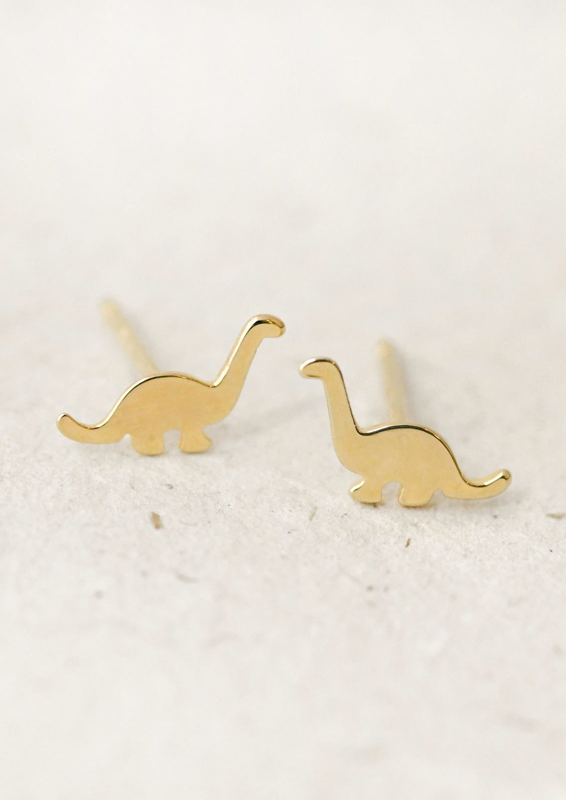 A pair of gold dinosaur stud earrings.