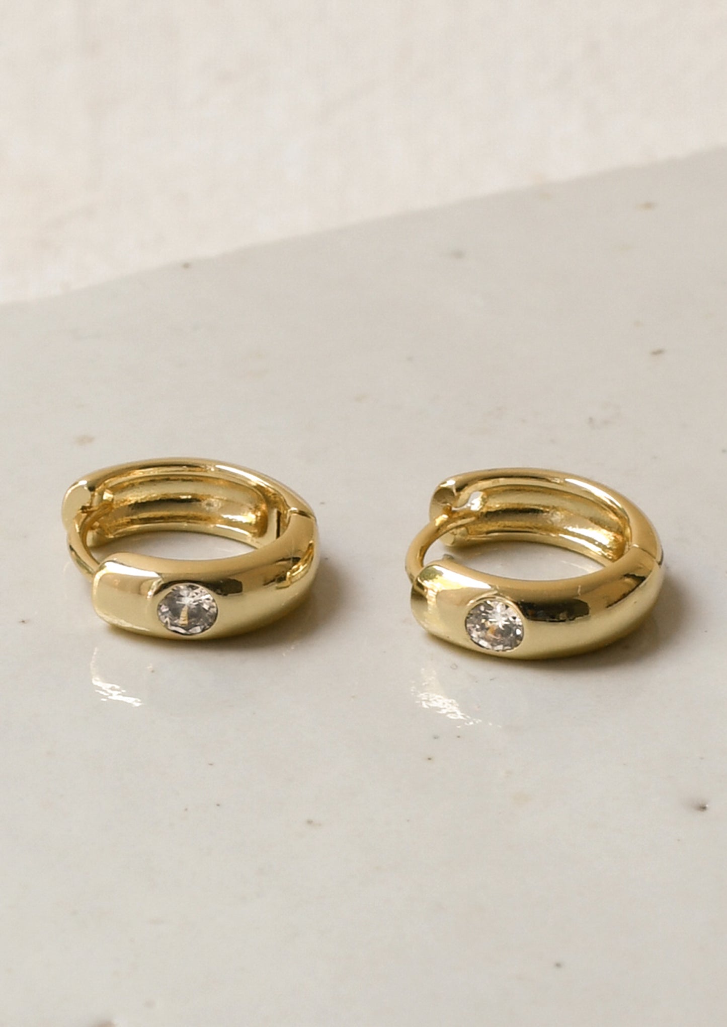 A pair of gold hoop earrings with a round diamond on the front.