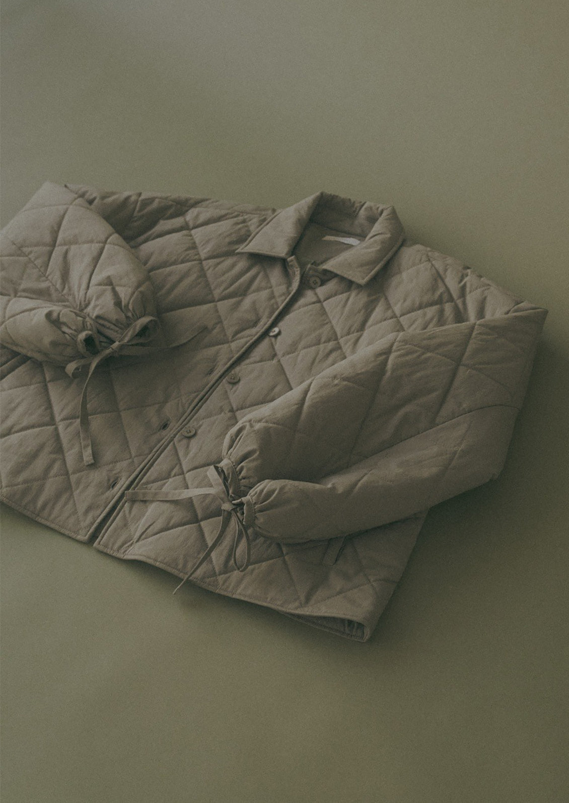 A woman wearing a quilted, padded jacket in army green with tie detail at wrists.