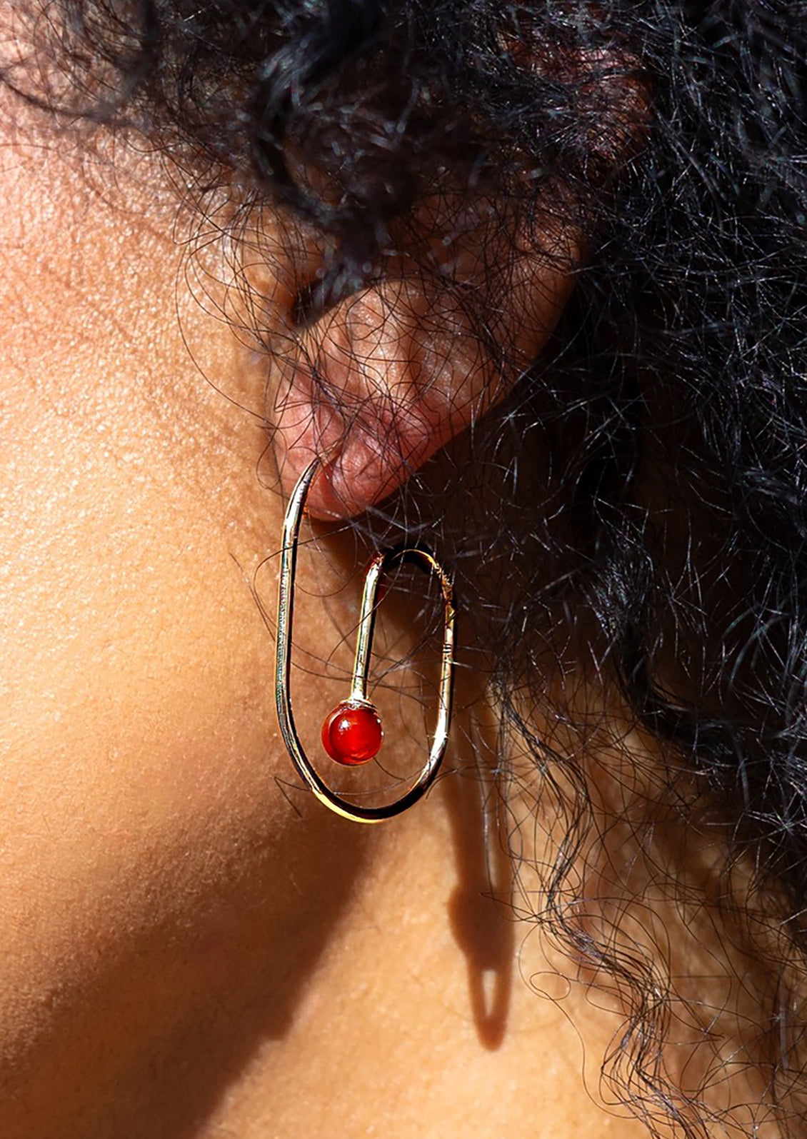 A pair of gold loop shaped hoop earrings with red gemstone at middle.