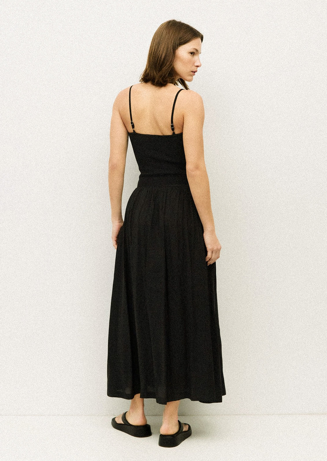 A woman wearing a black spaghetti strap dress with fitted bodice.