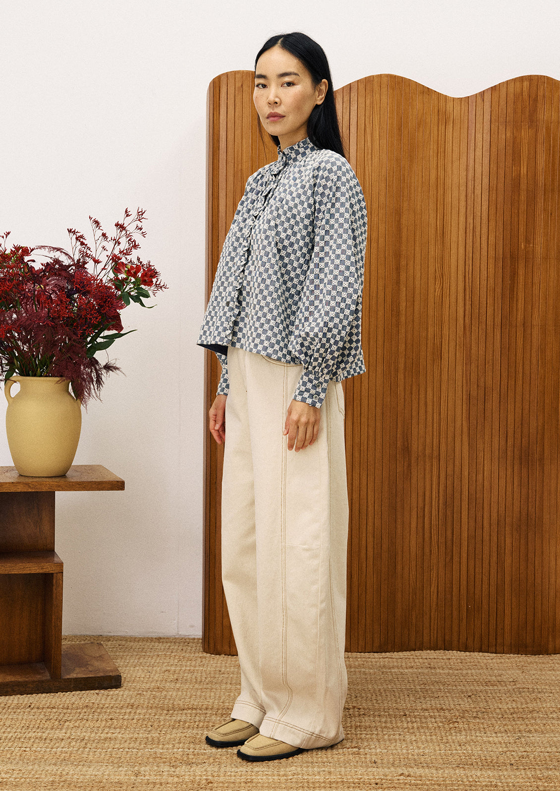 A woman wearing a ruffle neck blouse with embroidered white check pattern.