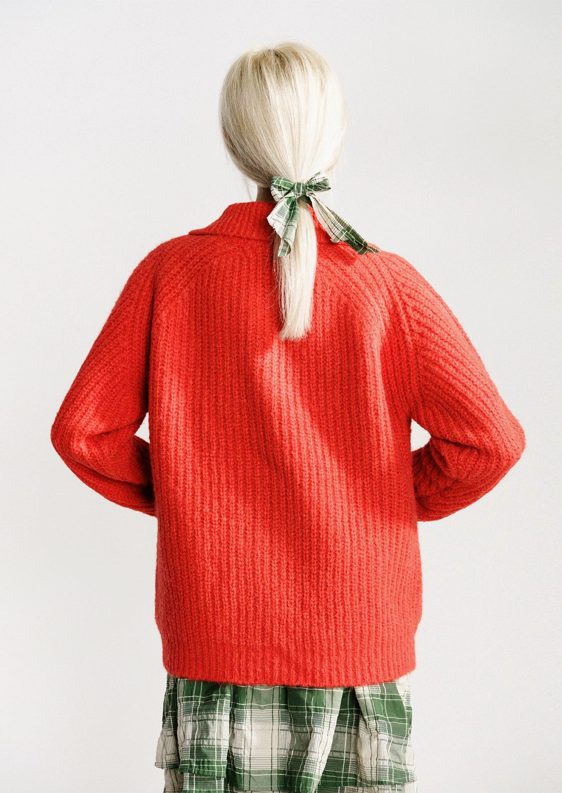A woman wearing a red-orange knit cardigan sweater.
