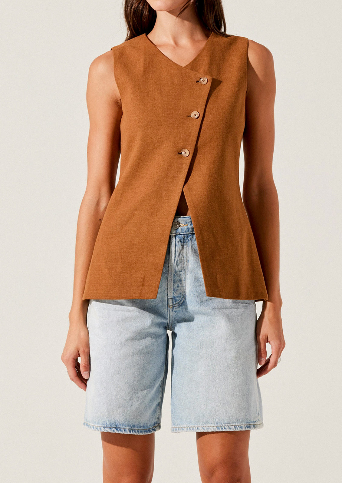 A person wearing a rust colored vest with asymmetrical button front closure.