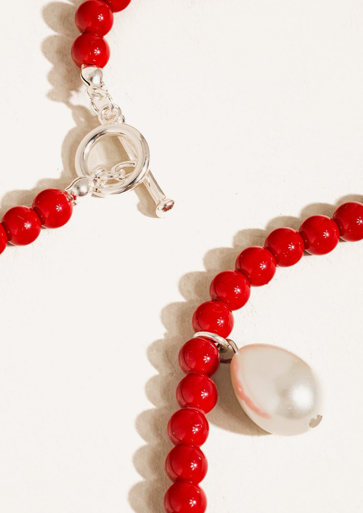 A red beaded necklace with silver hardware and pearl charm.