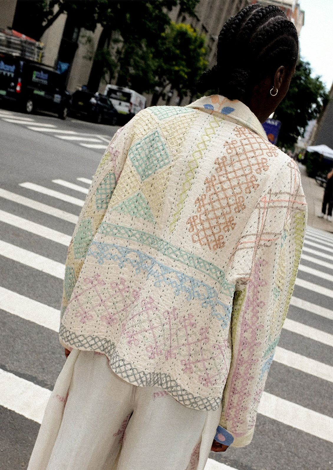 A person wearing a cream jacket with allover pastel embroidery.