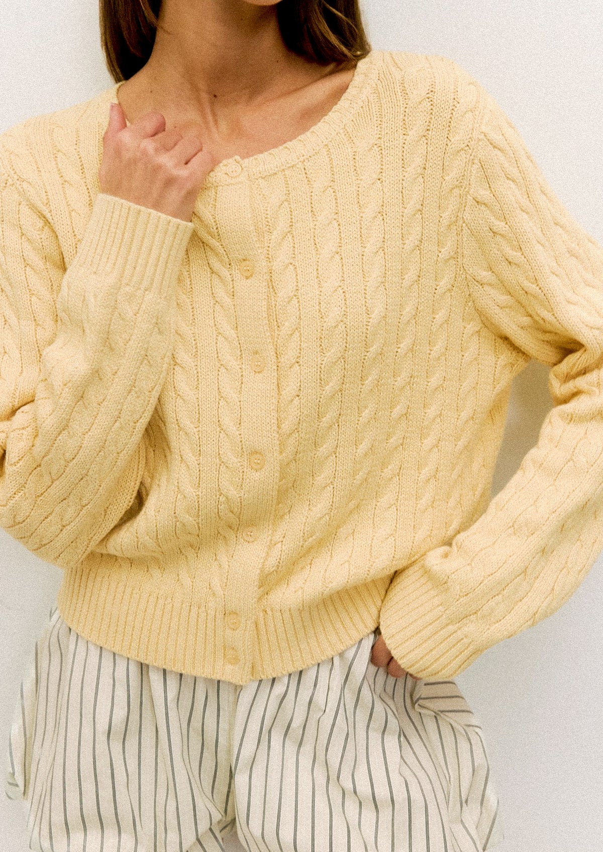 Person wearing a light yellow cable knit sweater against a plain background