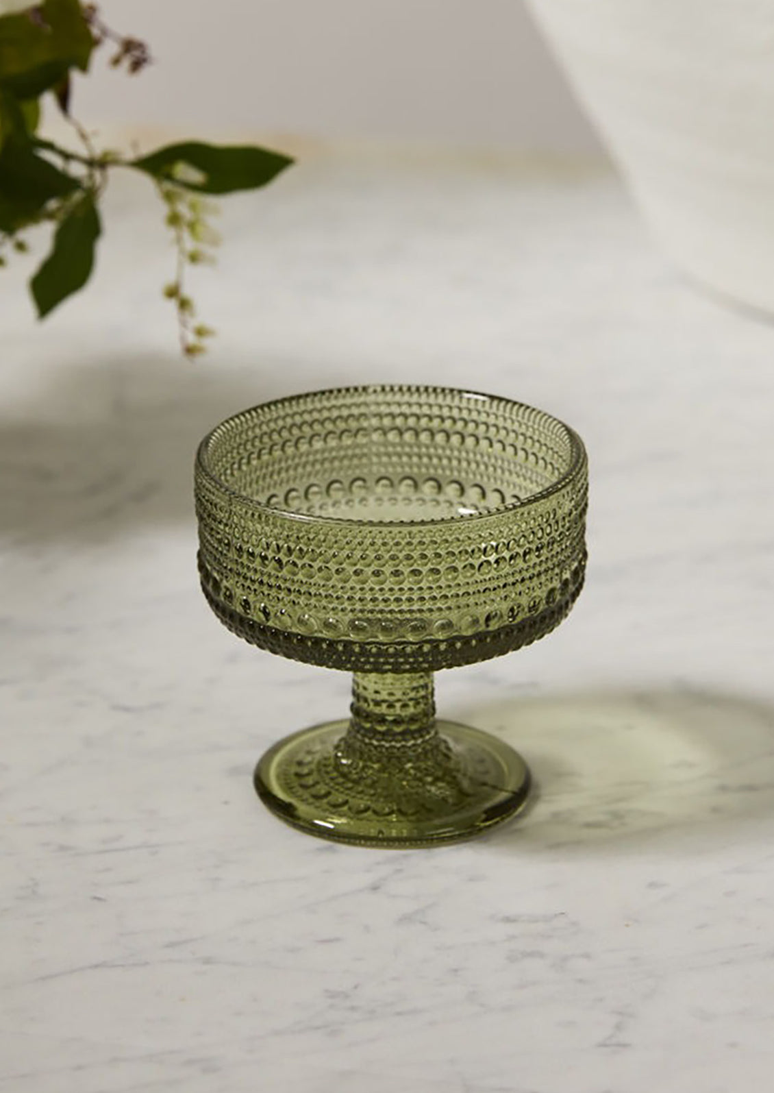 A coupe glass in olive green glass with round, vintage-style beaded texture.