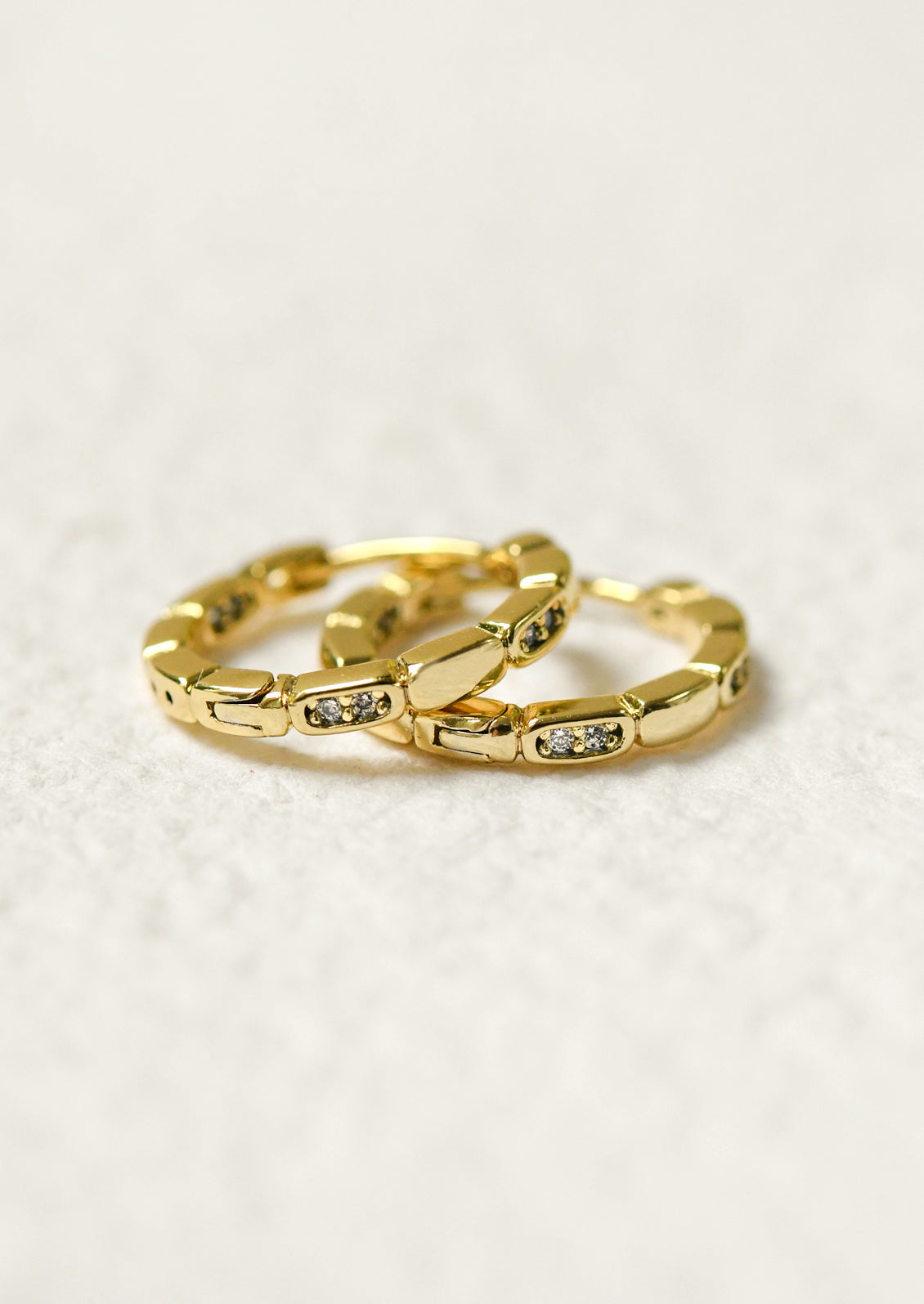 A pair of gold huggie hoop earrings with glass crystals.