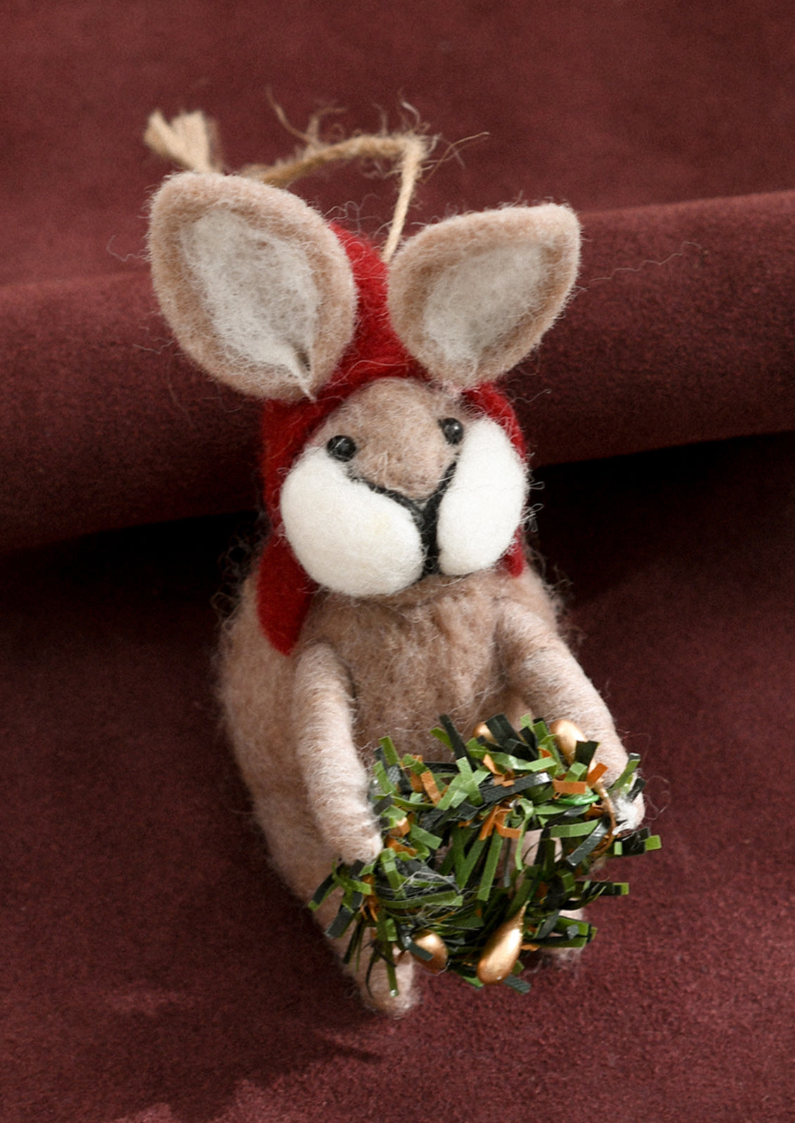A felted beige bunny ornament wearing red hood and carrying wreath.