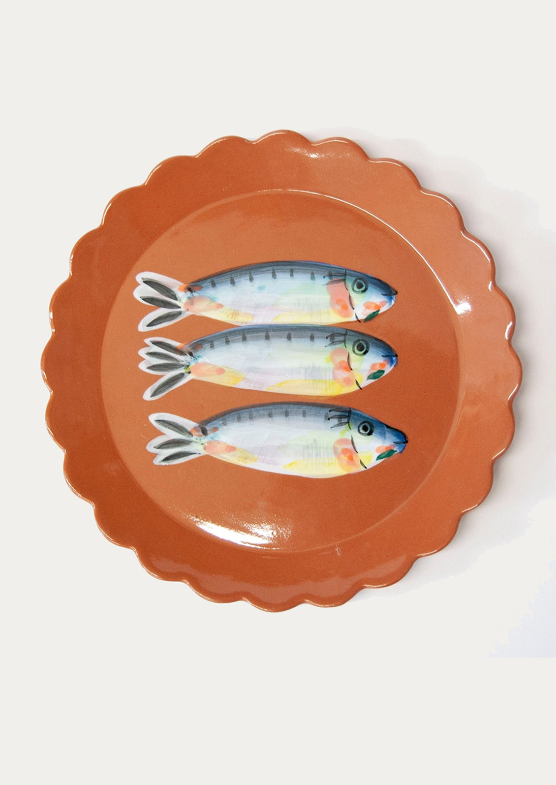 A terracotta plate with scalloped edges, with hand painted fish motif at center.