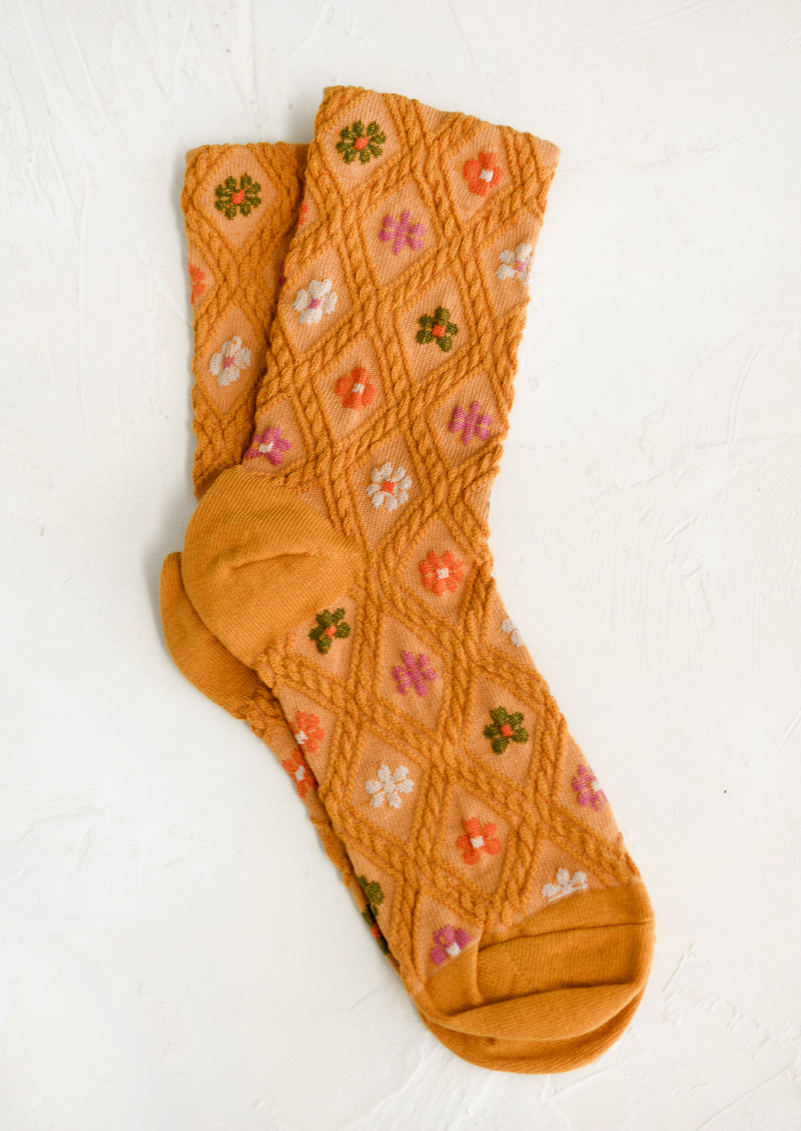 A pair of mustard socks with green, orange pink and white flowers.