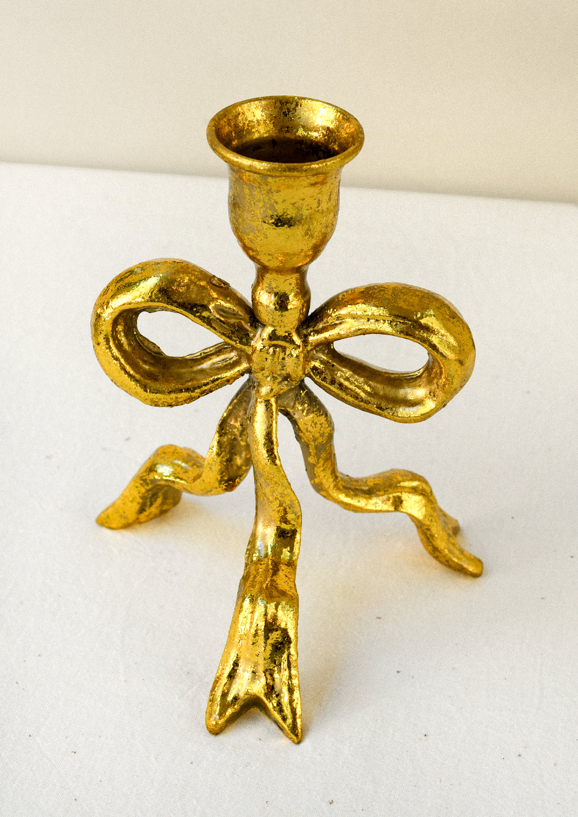 A metal taper holder in the shape of a bow with a gold finish.