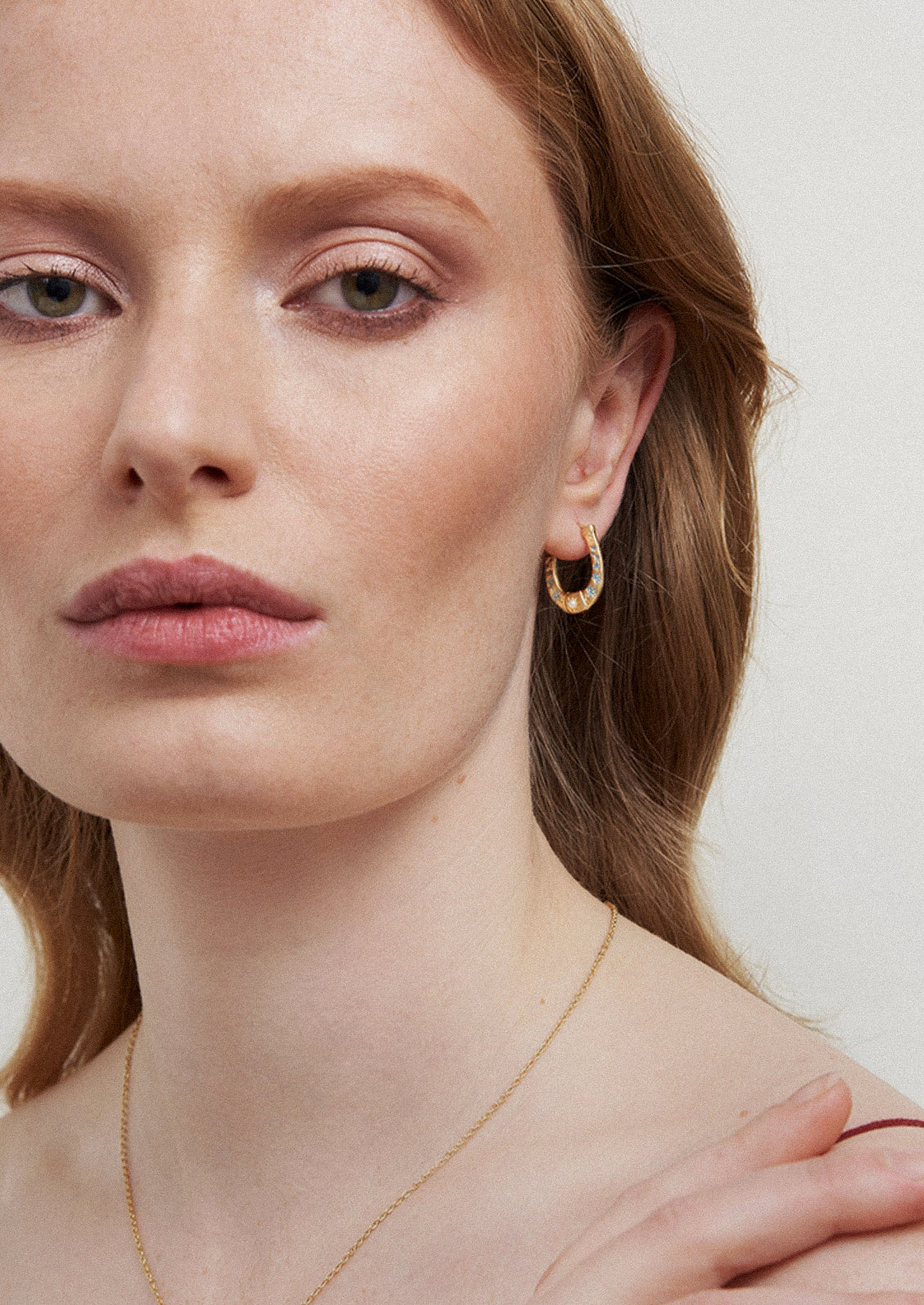 A woman wearing a gold horseshoe shaped earring.