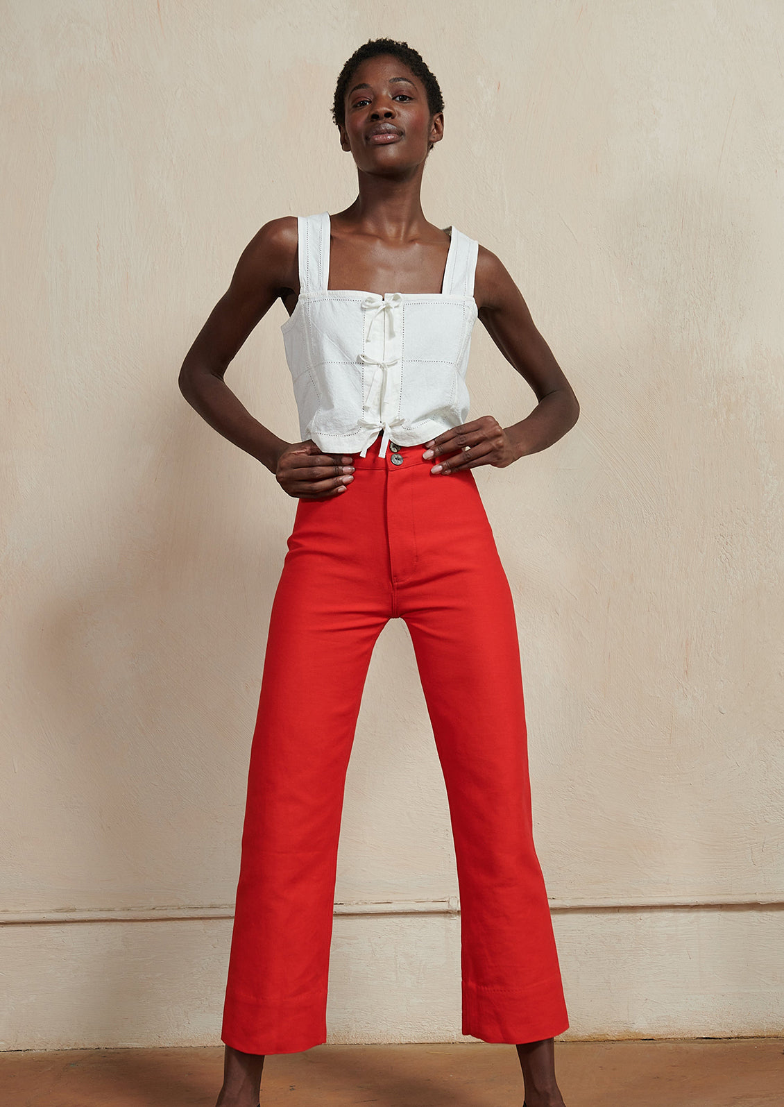 A woman wearing a white square neck tank and red pants.