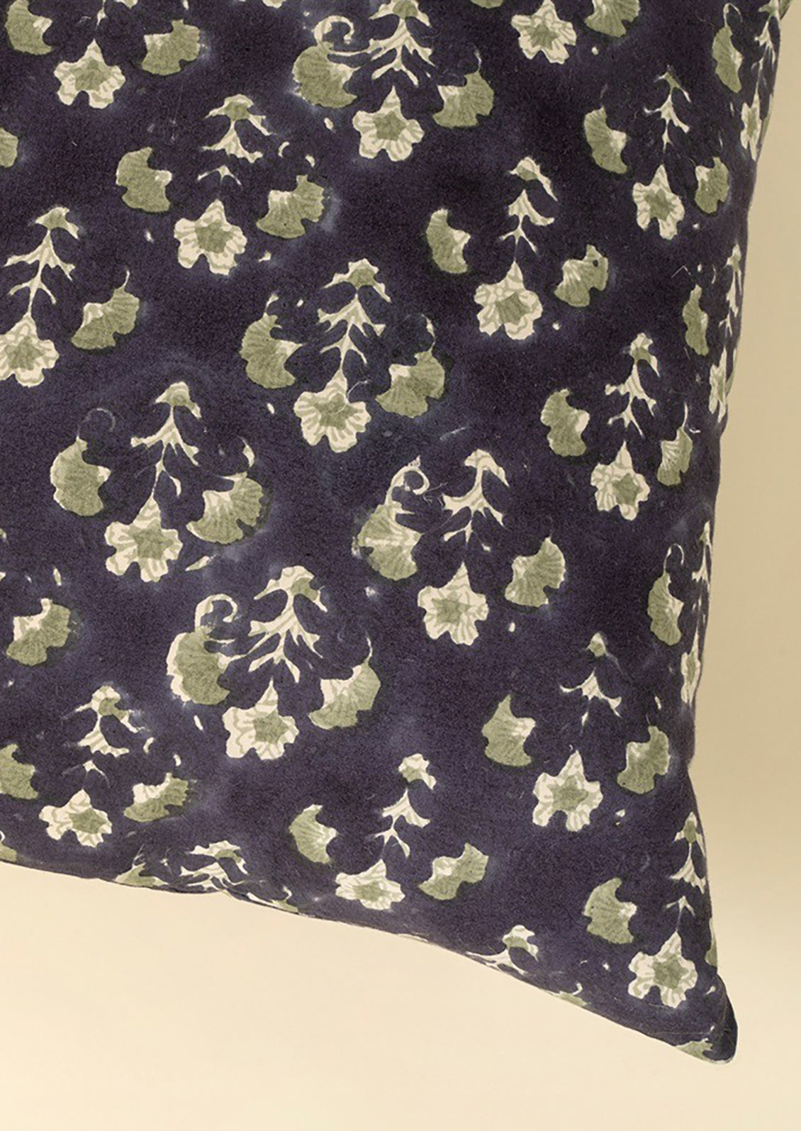 A block printed throw pillow with dark blue background and sage green floral print.