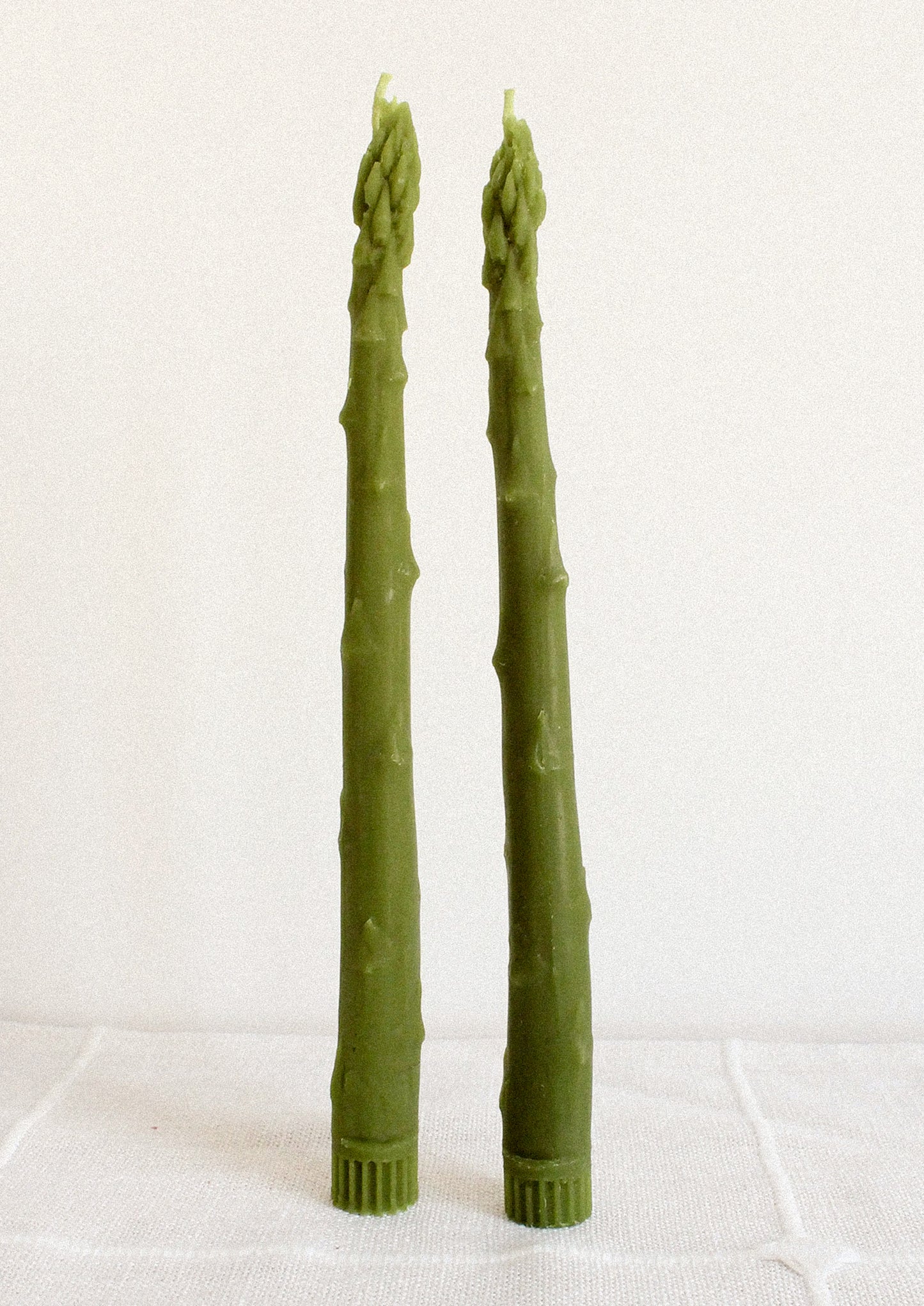 Two green asparagus shaped taper candles on a white background