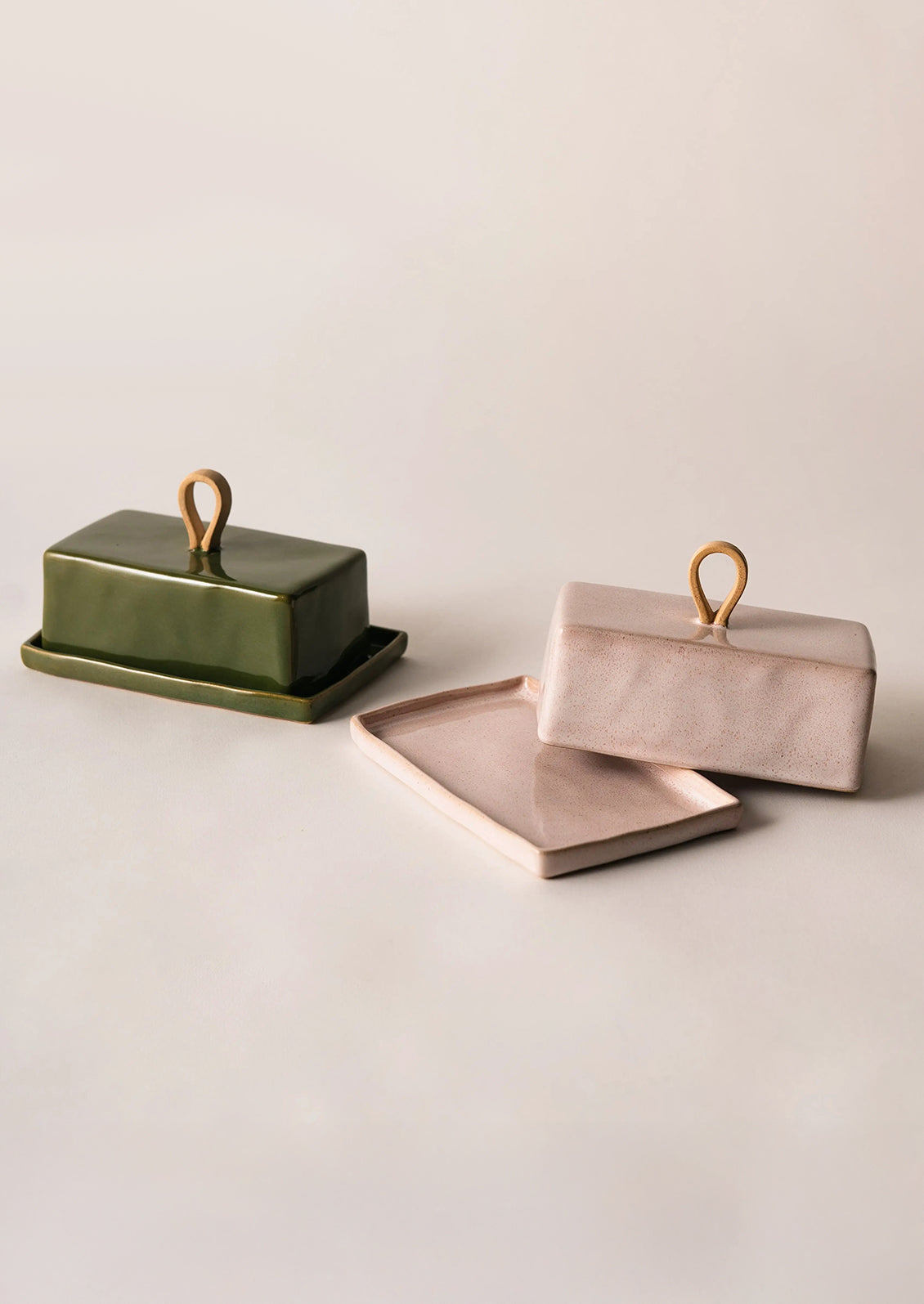 Two ceramic containers, one green and one pink, on a light beige surface.