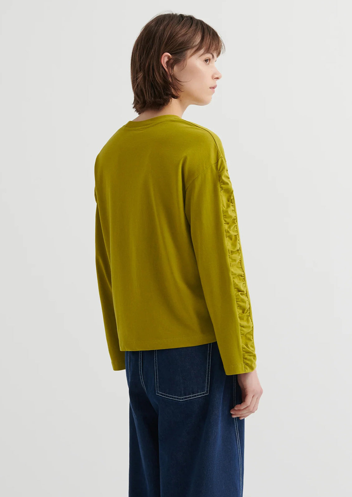 Person wearing a chartreuse long-sleeve shirt with a textured sleeve design on a white background