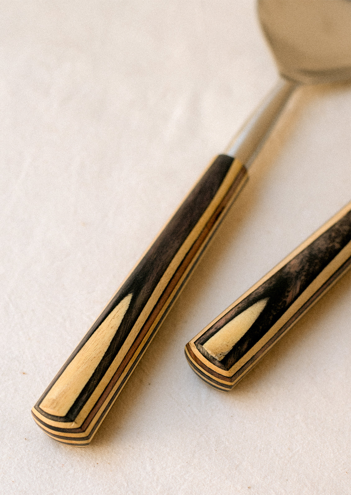 A pair of stainless steel, modern salad servers with two-tone wooden handle.
