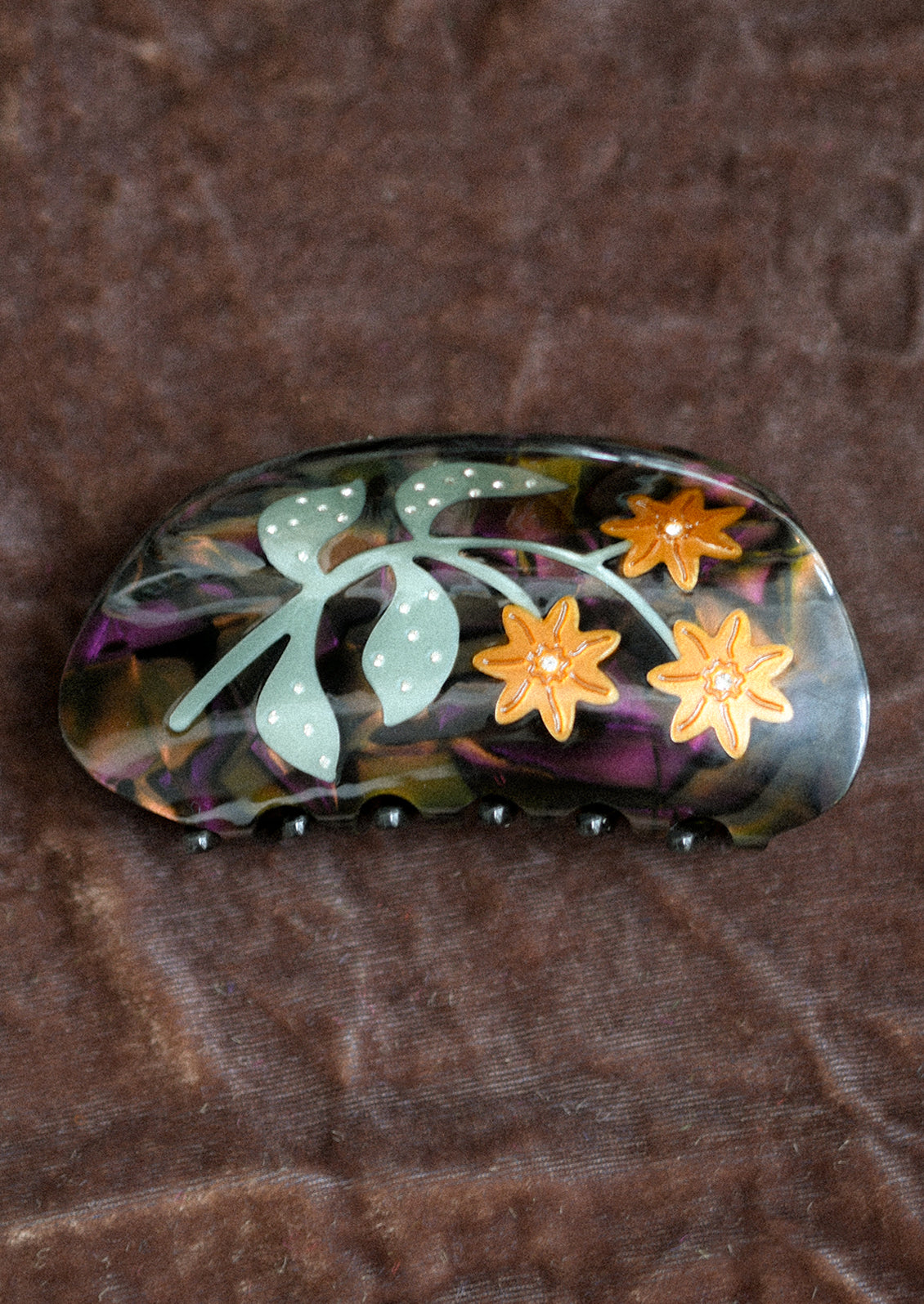 A dark purple hair claw with orange lady's mantle flower design.