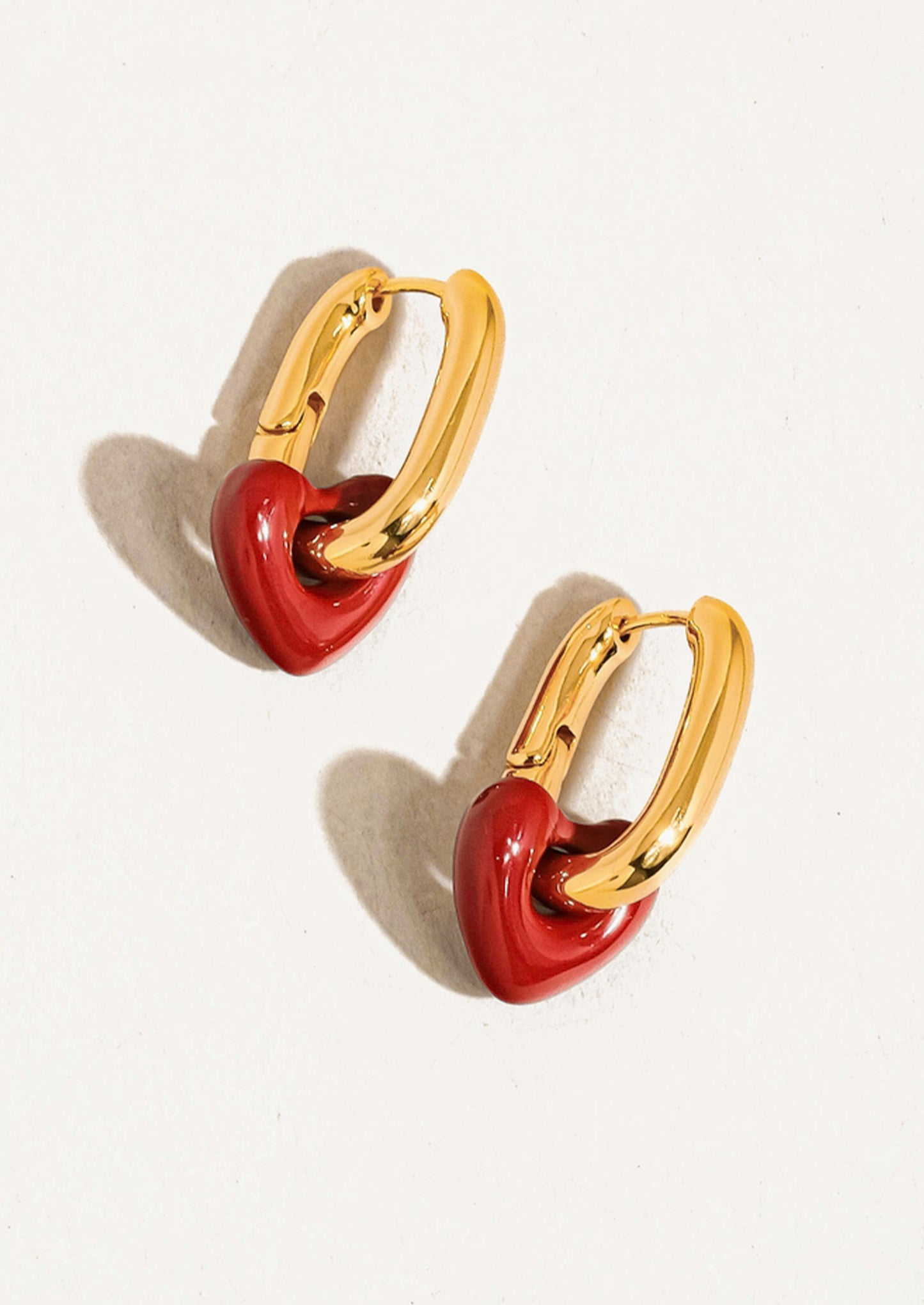 Pair of gold hoop earrings with red heart-shaped centers on a white background