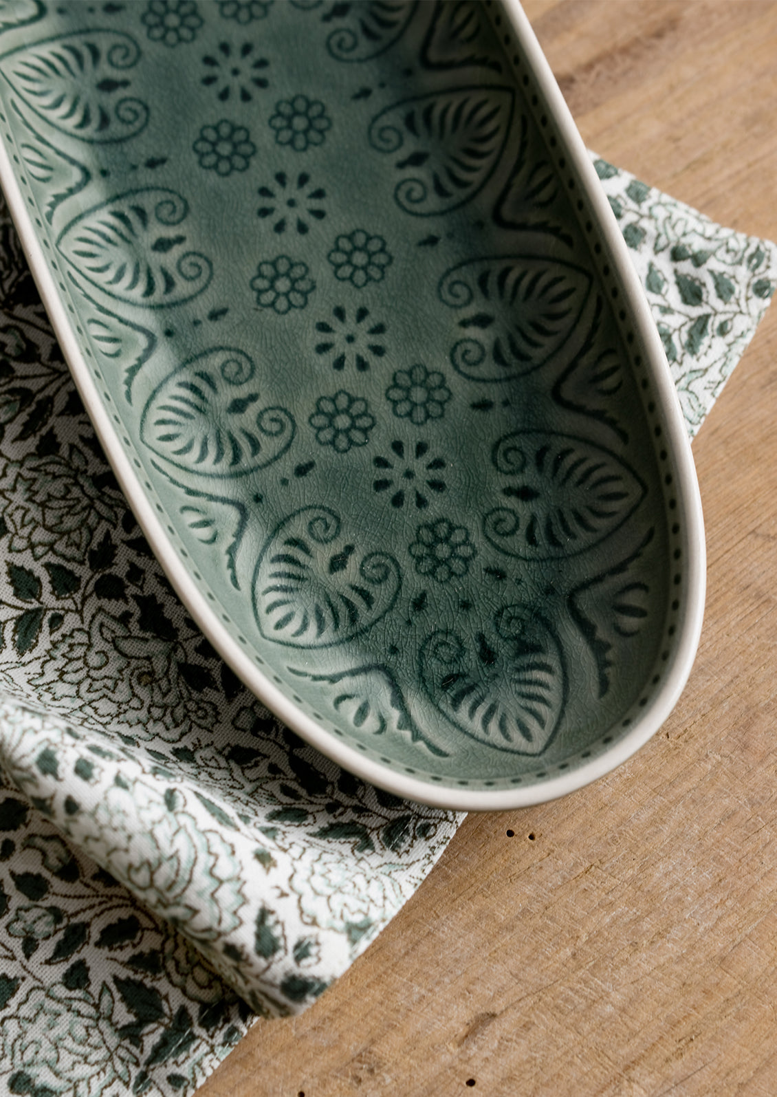 An oblong, curved platter in glossy green glaze with Polish inspired pattern.