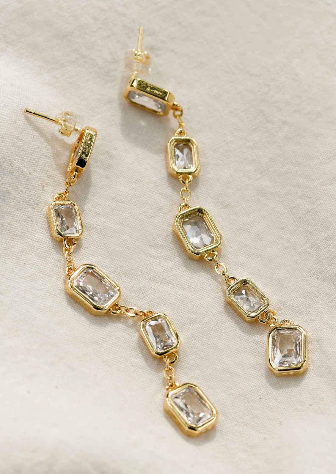 A pair of long gold dangling earrings with large rectangular gems.