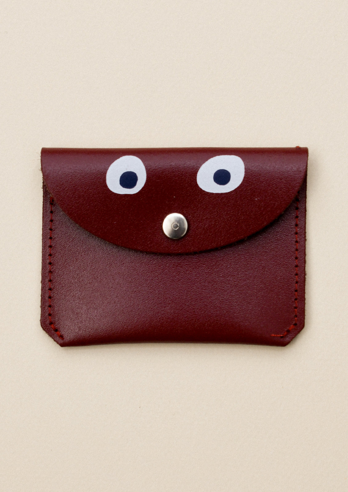 A brown leather flap front coin pouch with hand painted googly eye detail.