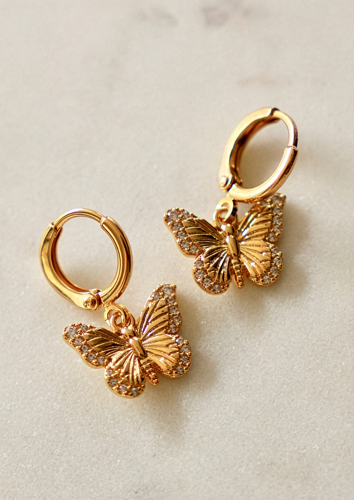 Gold butterfly earrings on a light beige background
