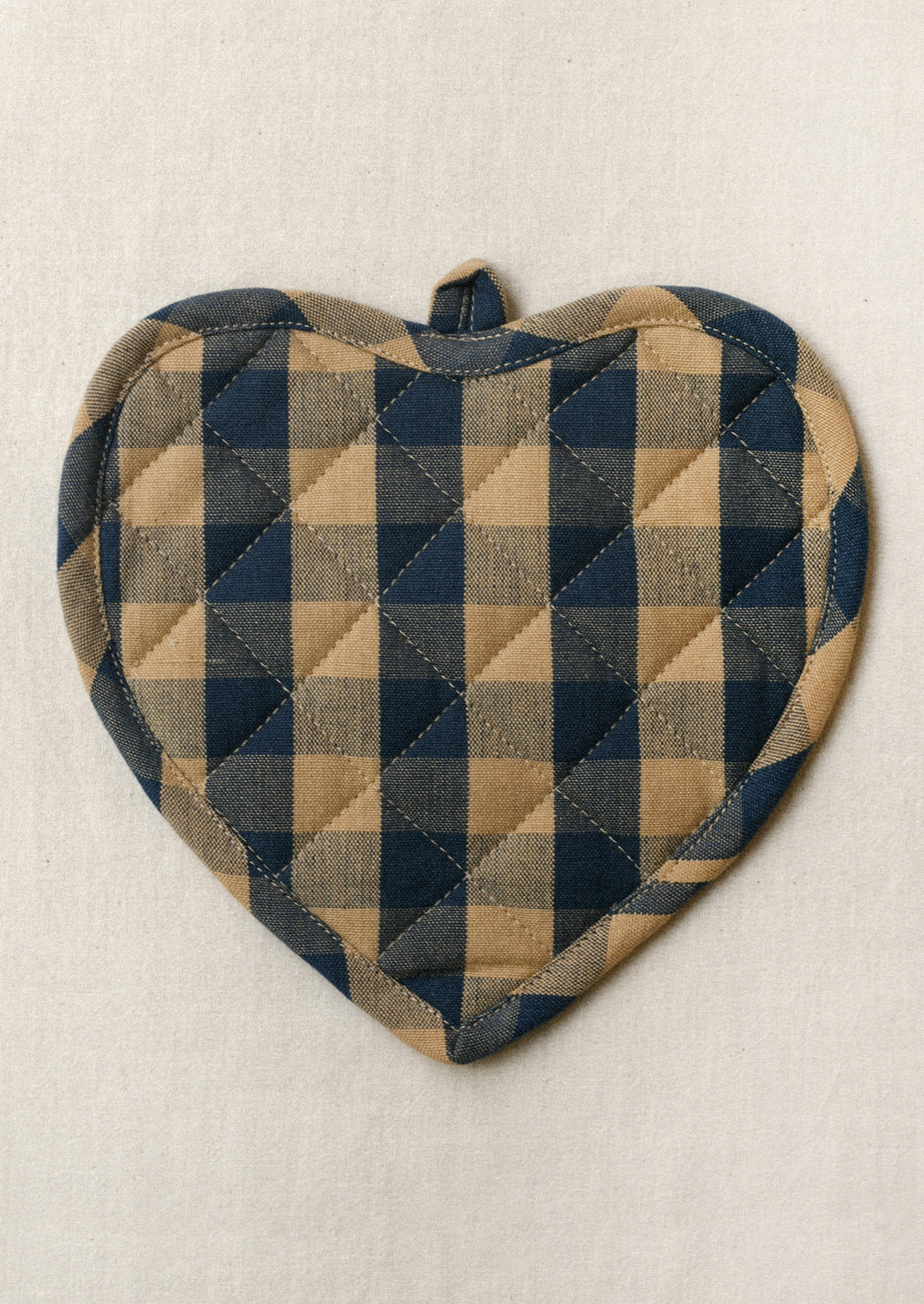 A heart shaped pot holder with a navy and tan gingham pattern.