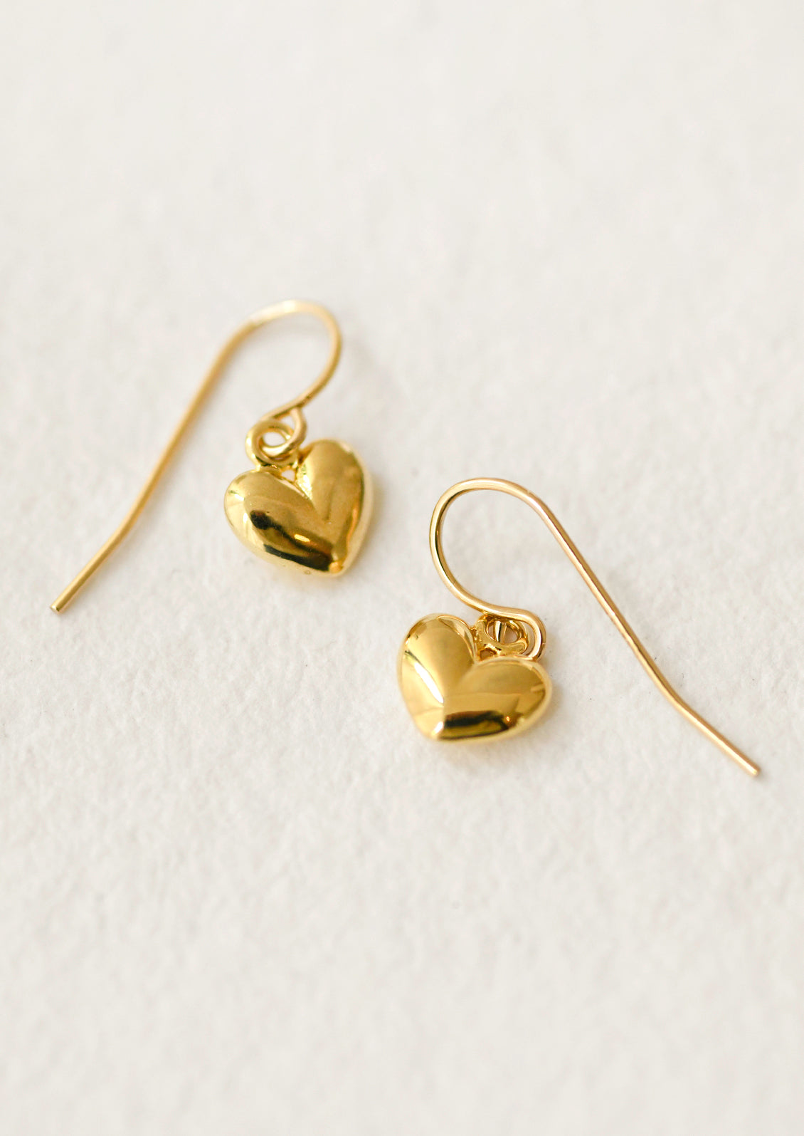 A pair of gold puffy heart dangling earrings.
