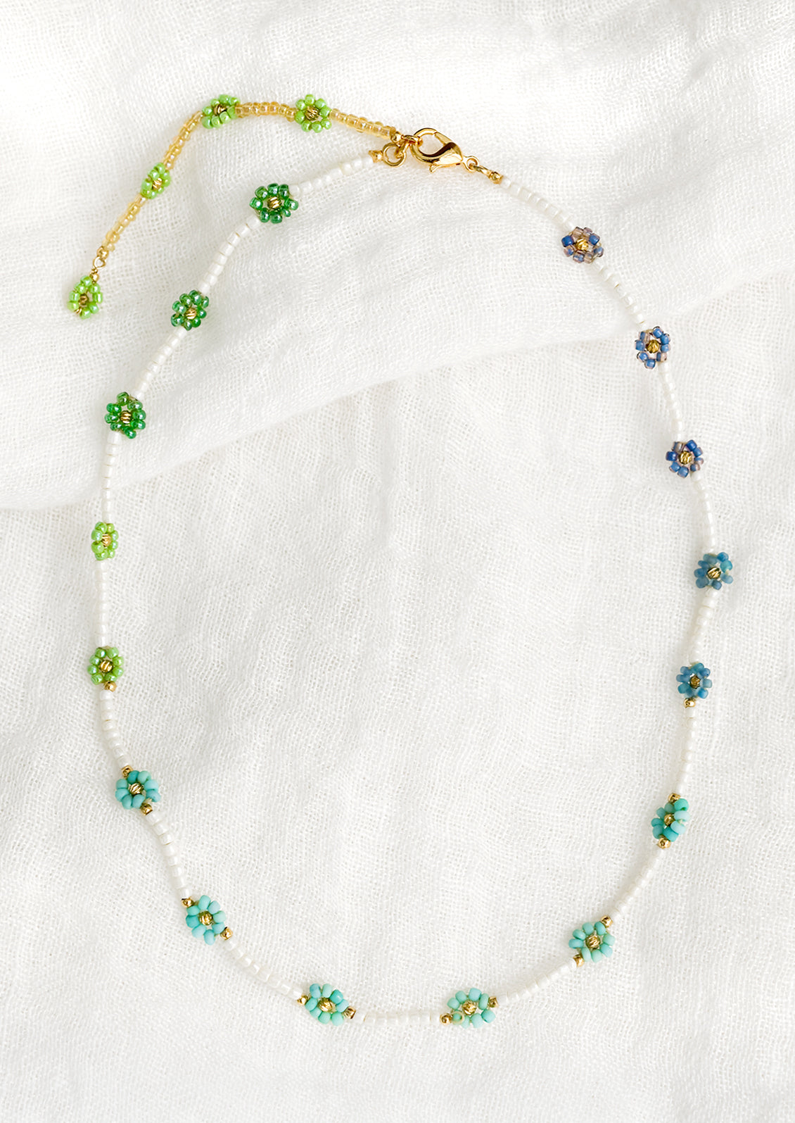 A beaded necklace with white beads and blue and green beaded flowers.